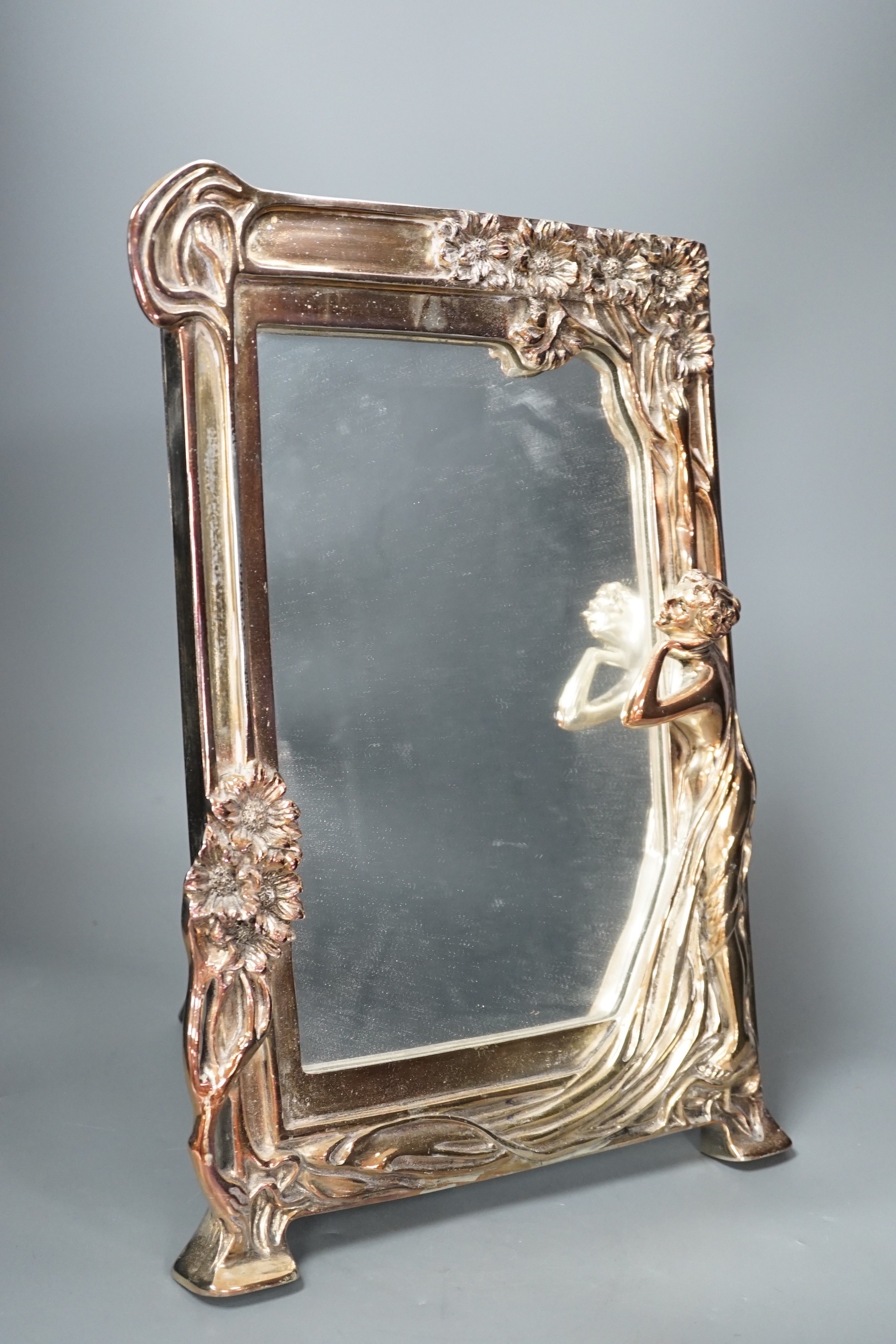 A silver plated Art Nouveau style mirrored frame, decorated with a female figure, tree and flowers in relief, 39.5cms high